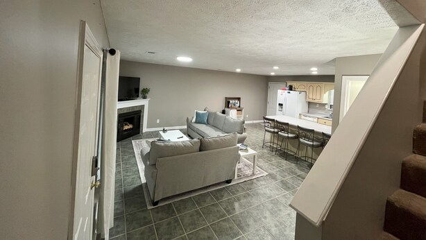 A spacious living room with a fireplace, a sofa, and a dining area with a kitchen in the background.