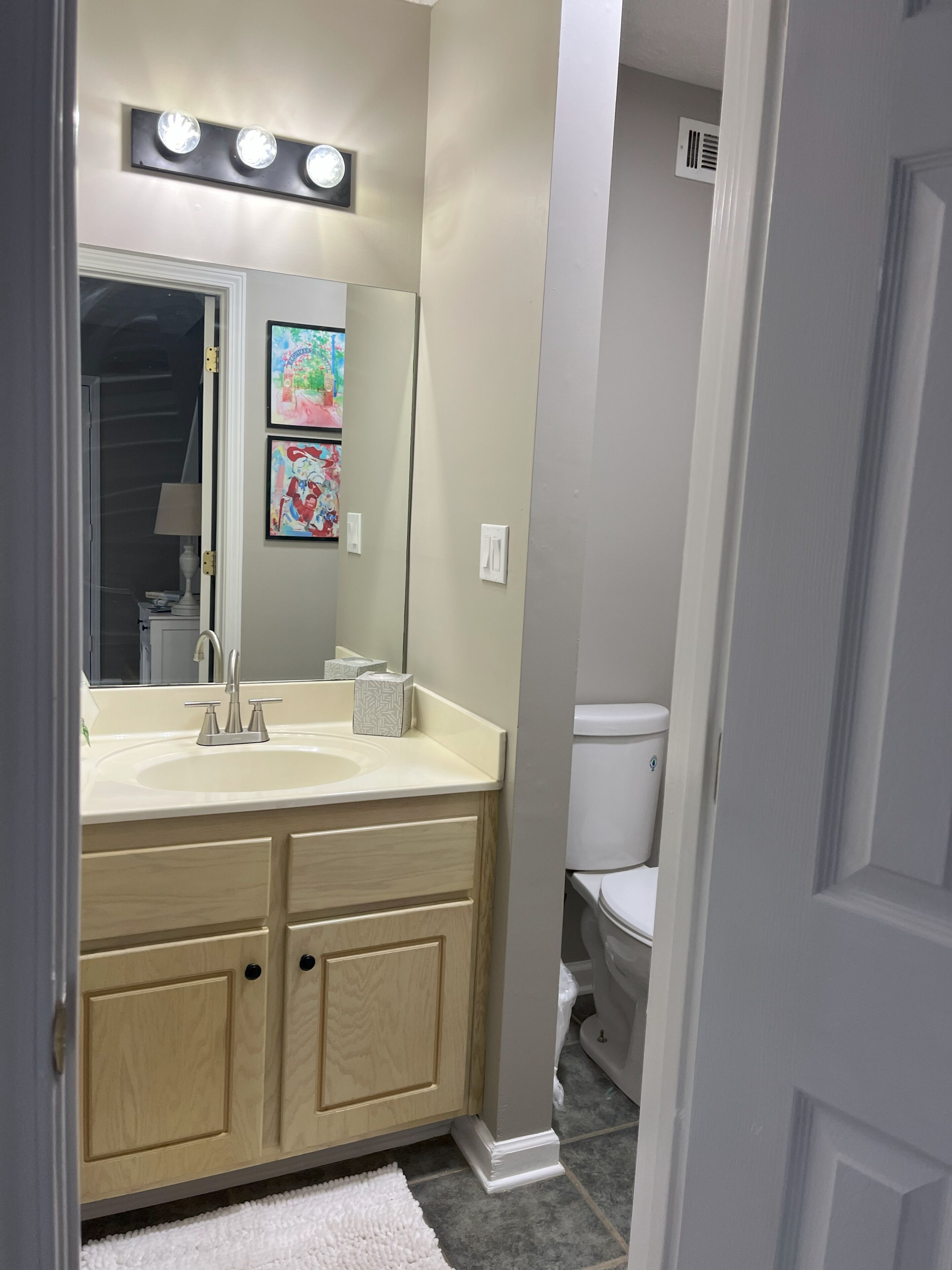 A bathroom with a double sink vanity, a mirror, a toilet, and a light fixture above the mirror.