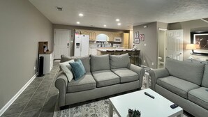 A modern living room with a grey sofa, a white coffee table, and a kitchen area in the background.