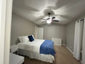 Un dormitorio con una cama, una mesita de noche, un aparador, un ventilador de techo y una puerta.