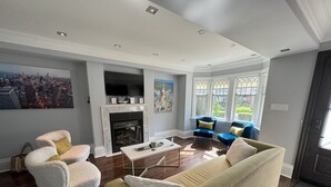 A living room with a fireplace, a television, and a large window with a view of the city. - Leaside Rental w/ Backyard& Pool, 3-bedroom house in fantastic Toronto (Toronto)