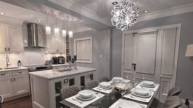 A modern kitchen with white cabinetry, a central island, and a dining area with a glass table set for four. - Leaside Rental w/ Backyard& Pool, 3-bedroom house in fantastic Toronto (Toronto)