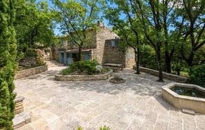 A stone courtyard with a stone house, a bench, and a small water feature. - Luxurious home in Goult (Goult)