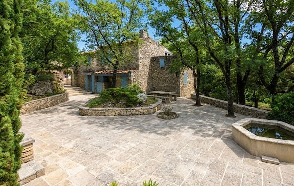 A stone courtyard with a stone house, a bench, and a small water feature. - Luxurious home in Goult (Goult)
