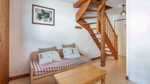 A cozy room with a wooden staircase, a sofa with checkered bedding, and a framed picture on the wall. - Apartment in Saint-Sorlin near Ski Resort (Saint-Sorlin-d´Arves)