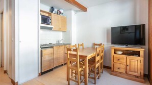 A compact kitchen with wooden cabinets, a dining table with chairs, and a television on a wooden stand. - Apartment in Saint-Sorlin near Ski Resort (Saint-Sorlin-d´Arves)