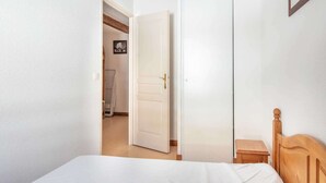 A bedroom with a bed, a wooden headboard, a small wooden nightstand, and a door leading to a bathroom. - Apartment in Saint-Sorlin near Ski Resort (Saint-Sorlin-d´Arves)