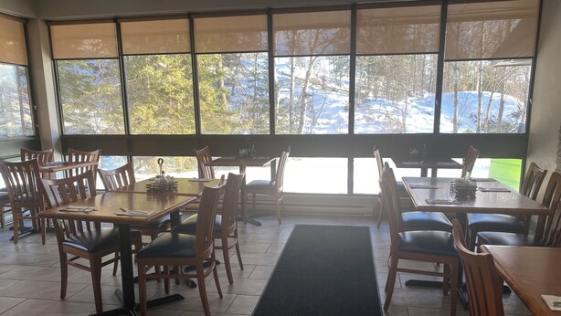 A restaurant with large windows, wooden tables, and chairs. - Sunset Inn Kenora (Kenora)