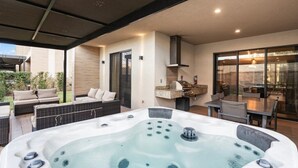 Ein moderner Außenbereich mit Whirlpool, einer Sitzecke, einem Grill und einer Glasdoor, die auf eine Terrasse führt.