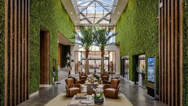 Eine großzügige Lobby mit hoher Decke, Wandverkleidungen in Grün und einer zentralen Sitzecke mit Ledersesseln und einem Couchtisch.