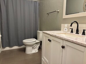 Un baño con inodoro, lavamanos con encimera de mármol y cortina de ducha.