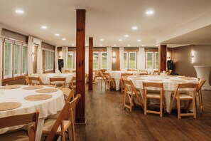 A spacious dining area with round tables, wooden chairs, and large windows offering views of the outdoors.