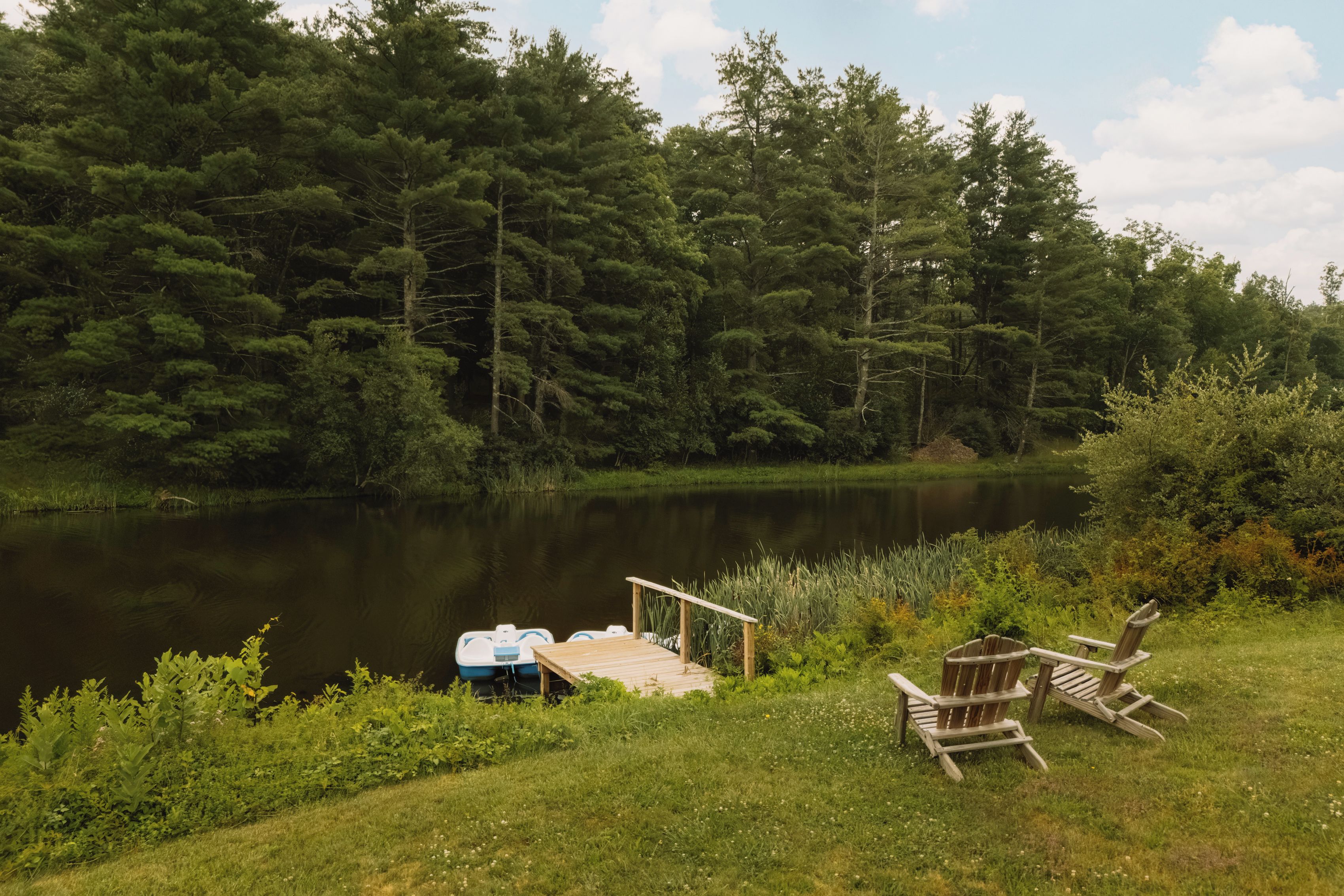 A lakeside setting with a dock, two chairs, and a rowboat.