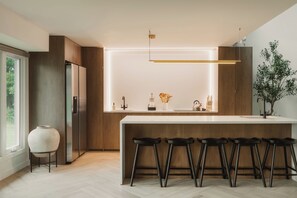 A modern kitchen with a central island, bar stools, a refrigerator, and a potted plant. - Great Lodge at Carter Bridge Estate (East Durham)