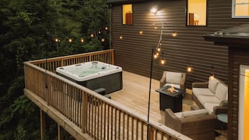 A deck with a hot tub, outdoor furniture, and string lights.