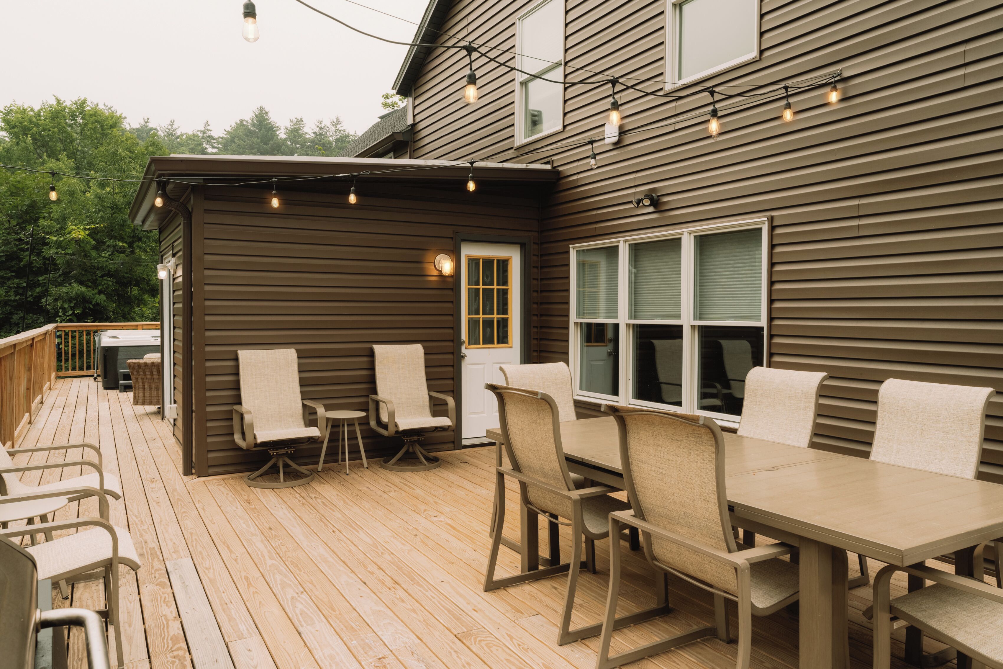 Eine Holzterrasse mit Gartenmöbeln, einem kleinen Gartenhaus und Lichterketten.