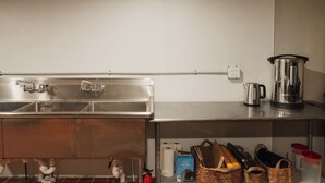 Een keuken met roestvrijstalen apparatuur, een spoelbak en een plank met manden en een waterkoker.