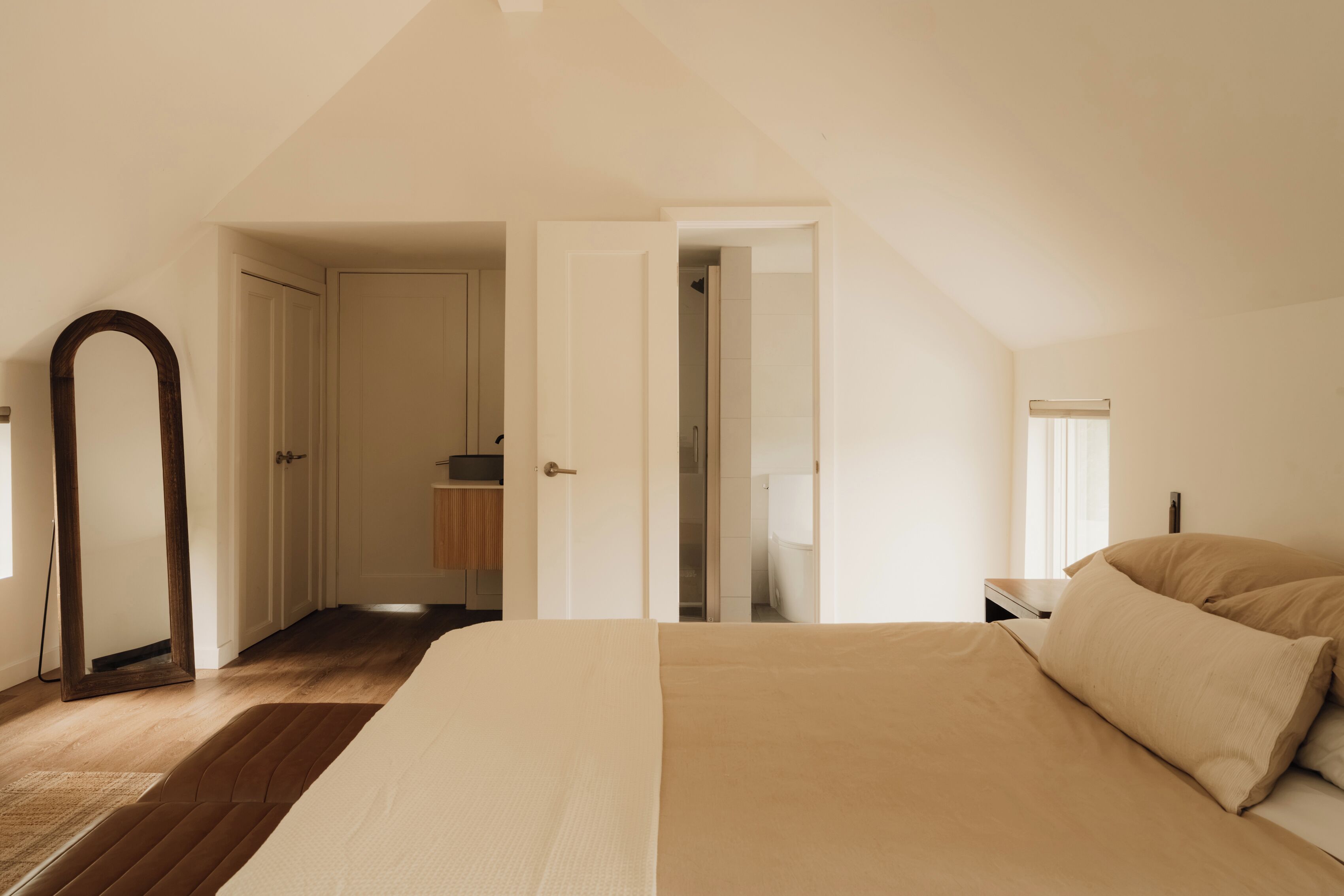 A bedroom with a large bed, a wooden floor, a wardrobe, and a mirror.