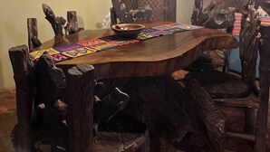 Een landelijke eethoek met een houten tafel en stoelen, een kleurrijke placemat en decoratieve muurkunst.