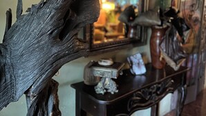 Een kamer met een groot houten beeld op de voorgrond, een spiegel aan de muur en een kleine tafel met diverse objecten.
