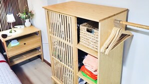A room with a wooden cabinet with shelves, a small table with a lamp, and a bed with a quilted cover.
