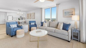 En moderne stue med sofa, lænestole, et sofabord og et spiseområde med en lysekrone.