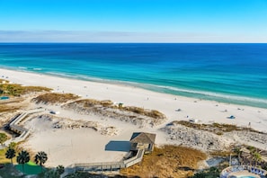 A beach with a wooden structure, a pool, and a sandy area with umbrellas.