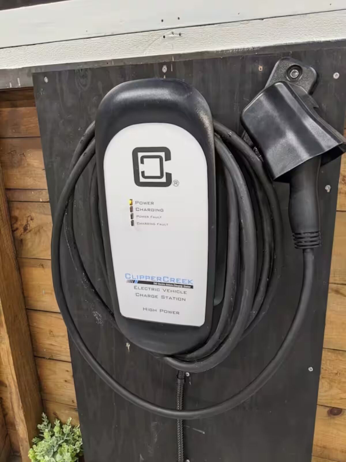 Uma estação de carregamento para veículos elétricos pretos, com etiqueta branca, cabo e tomada.