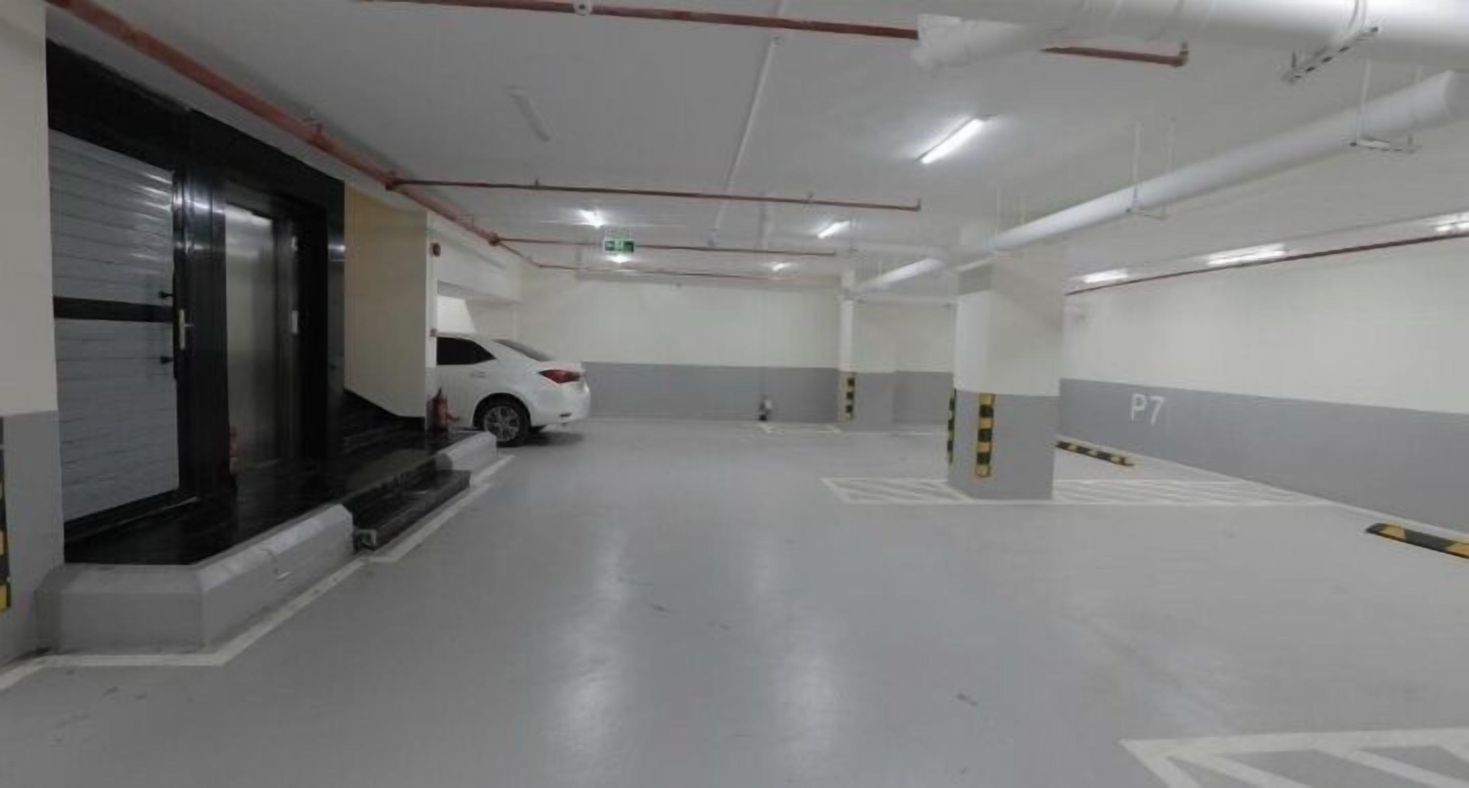 A parking garage with white walls, grey floor markings, and a white car parked in one of the bays.