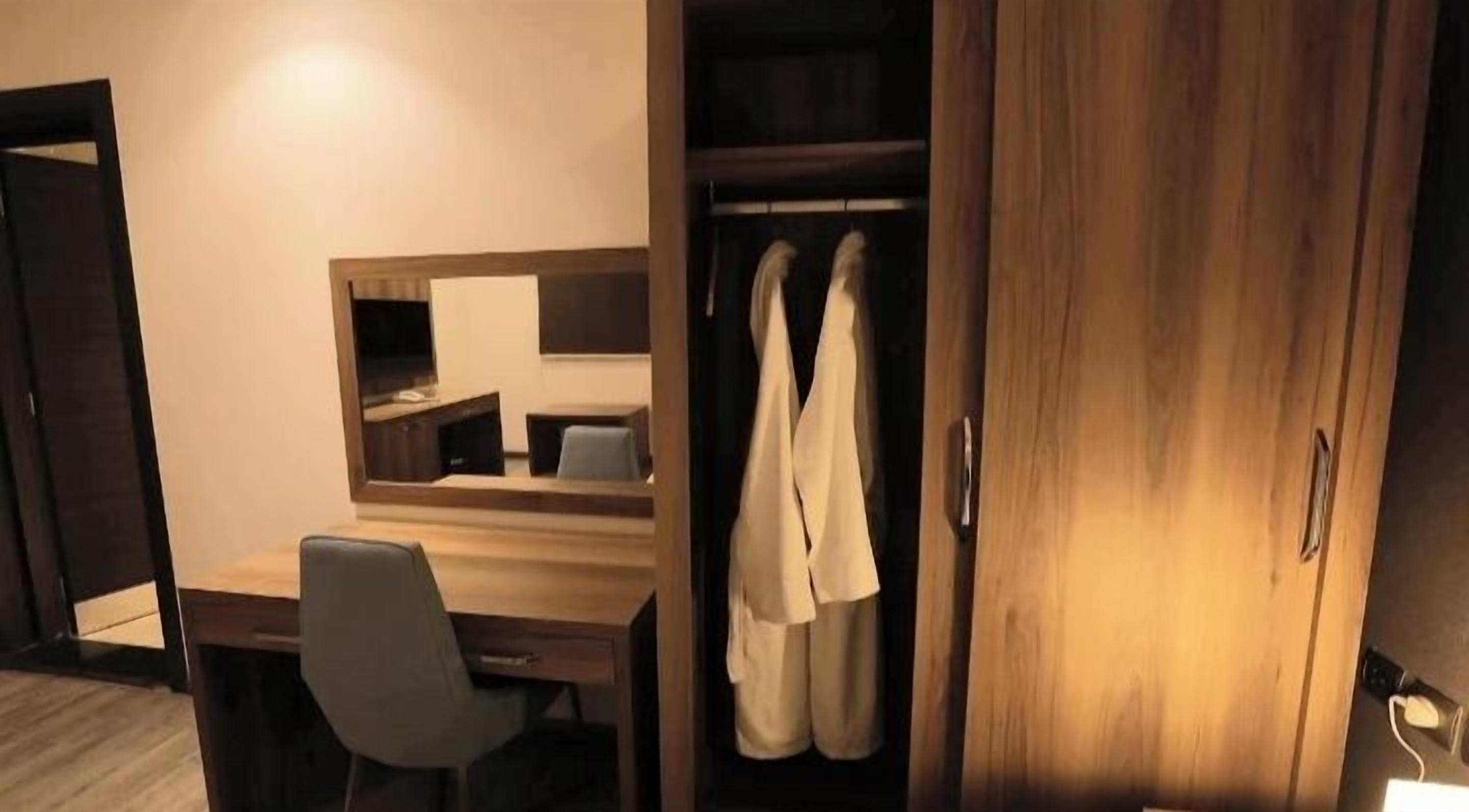 Habitación de hotel con escritorio de madera, una silla, un espejo y un armario con albornoces.