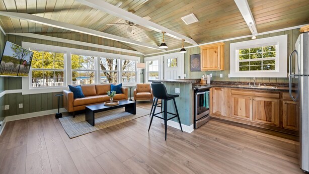 A spacious living area with a wooden ceiling, large windows, a kitchen with wooden cabinets, and a bar area. - Harbor Cottage | Downtown Fish Creek-Dog Friendly (Fish Creek)