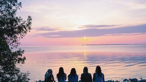 A group of people sitting on a rocky shore at sunset. - Harbor Cottage | Downtown Fish Creek-Dog Friendly (Fish Creek)