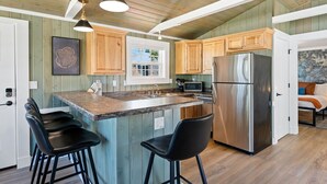 A kitchen with wooden cabinets, a stainless steel refrigerator, a microwave, and a large island with bar stools. - Harbor Cottage | Downtown Fish Creek-Dog Friendly (Fish Creek)