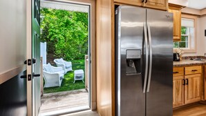 Une cuisine moderne avec des meubles en bois, un réfrigérateur en acier inoxydable et une porte-fenêtre coulissante donnant sur un patio aménagé avec du mobilier d’extérieur.