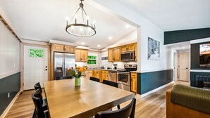 Une cuisine moderne avec des meubles en bois, des appareils en acier inoxydable et un coin repas comprenant une table et des chaises en bois.