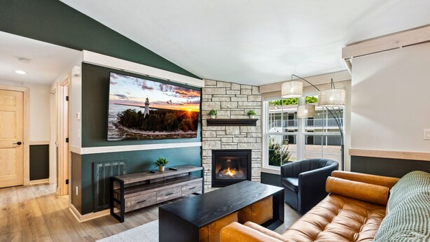 Un salon moderne avec une cheminée en pierre, un grand téléviseur à écran plat fixé au mur, un confortable canapé en cuir et une table basse en bois.