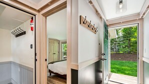A modern interior with a bed, a fire extinguisher, and a view of a green lawn through an open door. - Spruce Suite | Downtown Fish Creek~Dog-friendly (Fish Creek)
