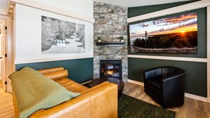 A cozy living room with a stone fireplace, a large framed black and white photograph, and a scenic sunset view on the wall. - Spruce Suite | Downtown Fish Creek~Dog-friendly (Fish Creek)
