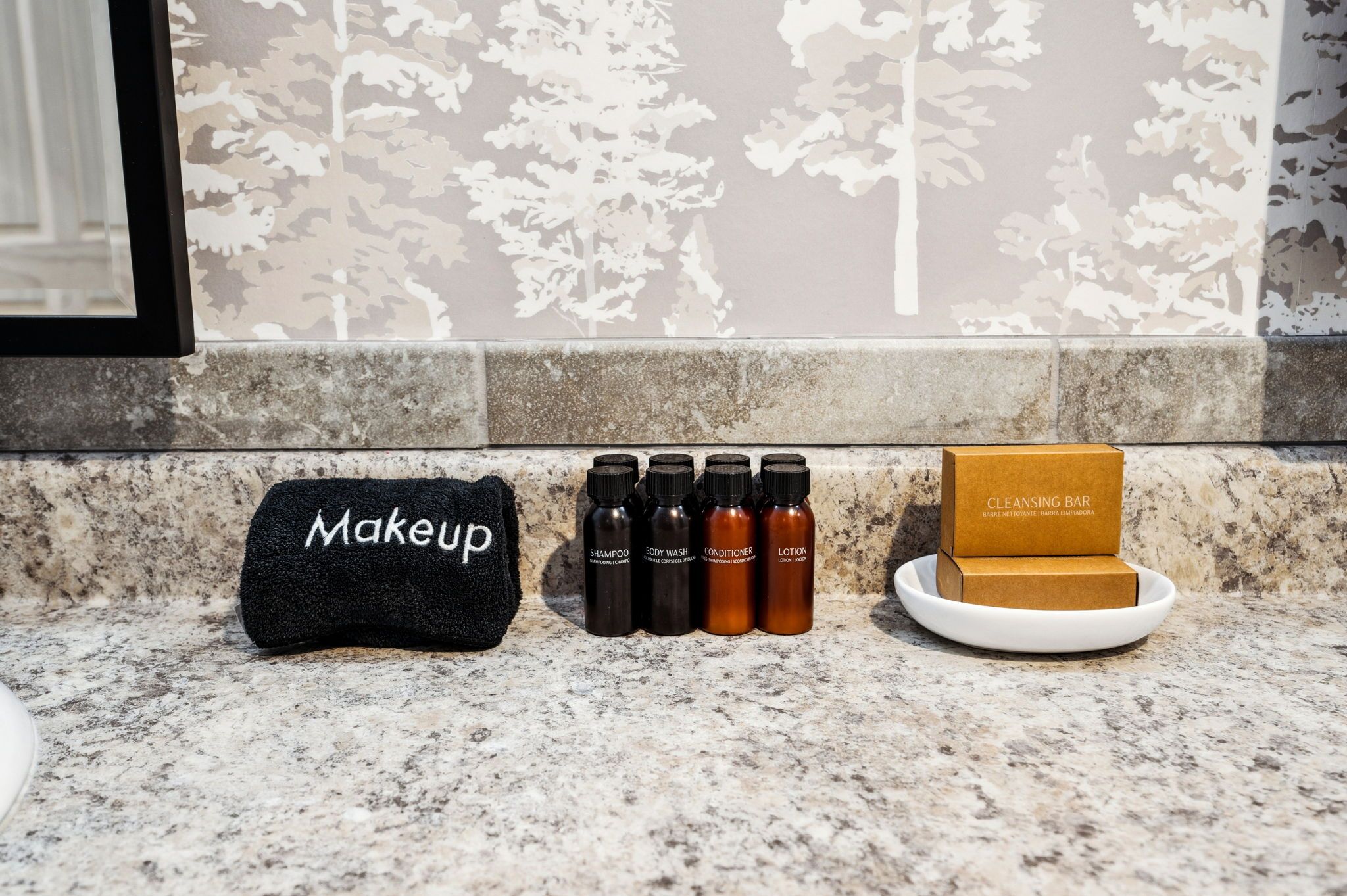 A bathroom vanity with a makeup bag, four bottles of skincare products, and a cleansing bar on a marble countertop.
