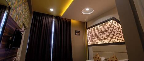 A modern hotel room with a neatly made bed, a television, and a decorative wall panel.