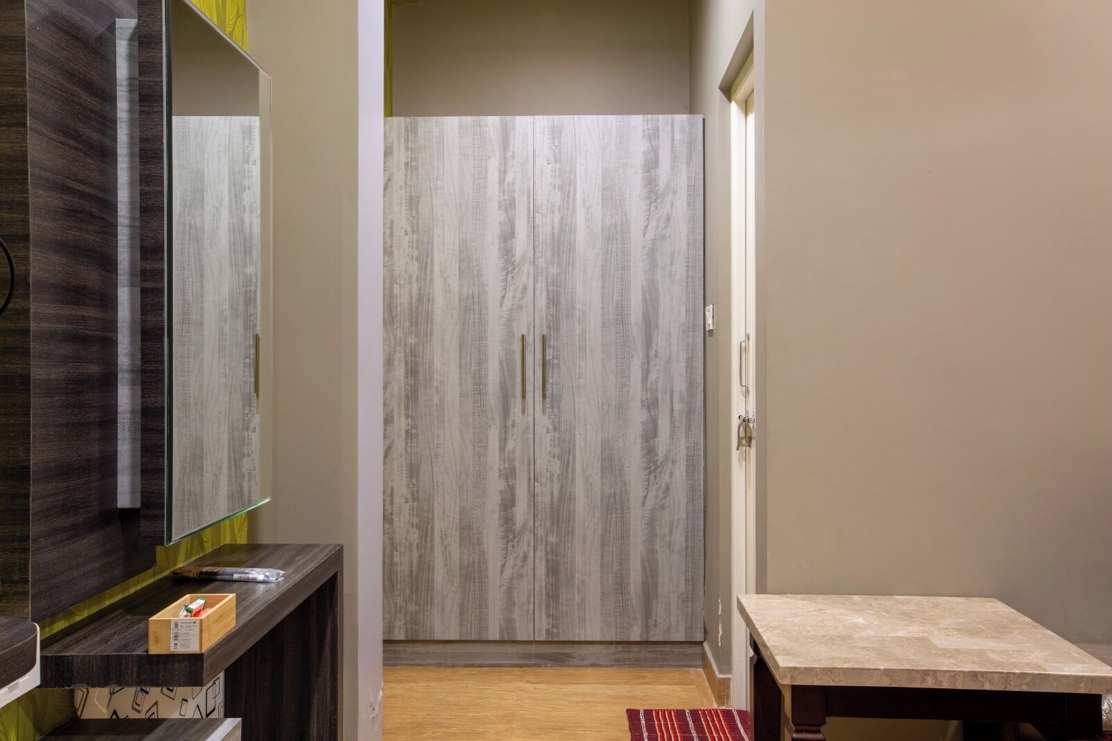 A hallway with a wooden wardrobe, a mirror, a small table, and a red rug.