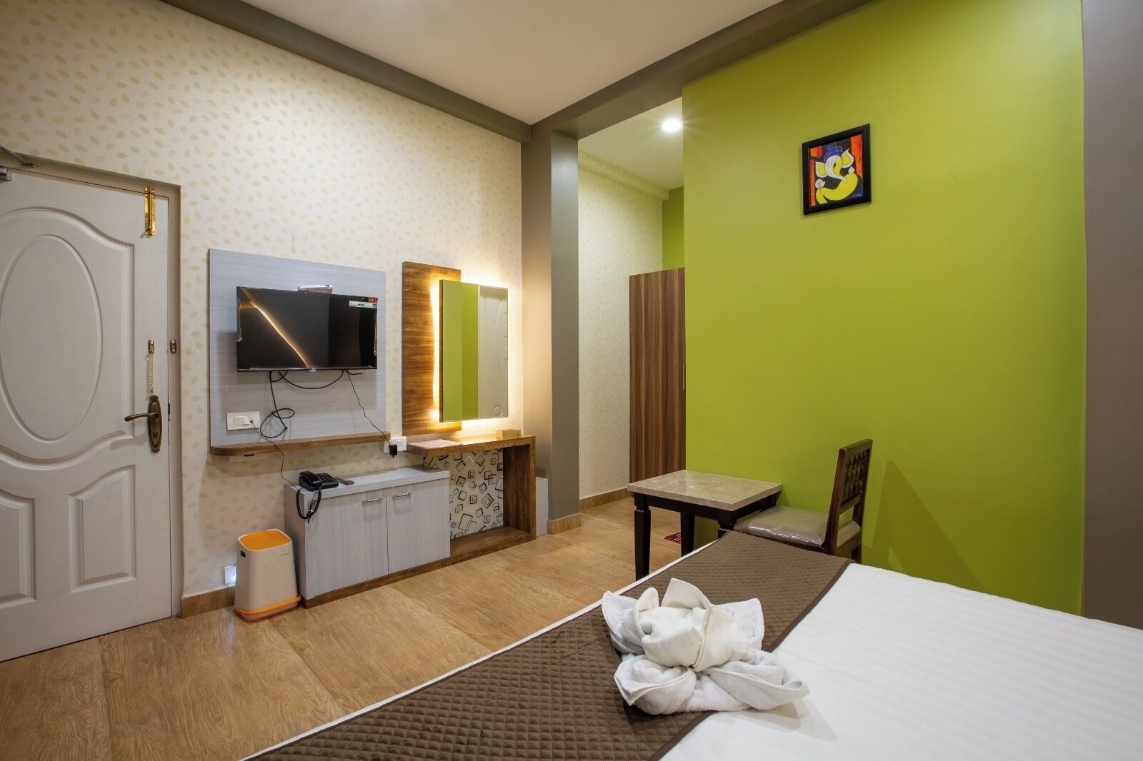 Habitación de hotel con cama, escritorio, silla, televisor, espejo y puerta del baño.