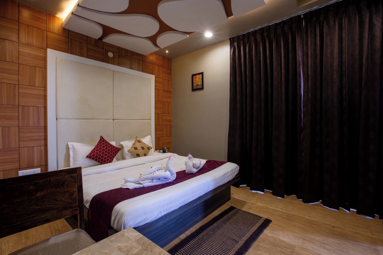 A hotel room with a wooden panel wall, a large bed with white bedding, a red pillow, and a black curtain.
