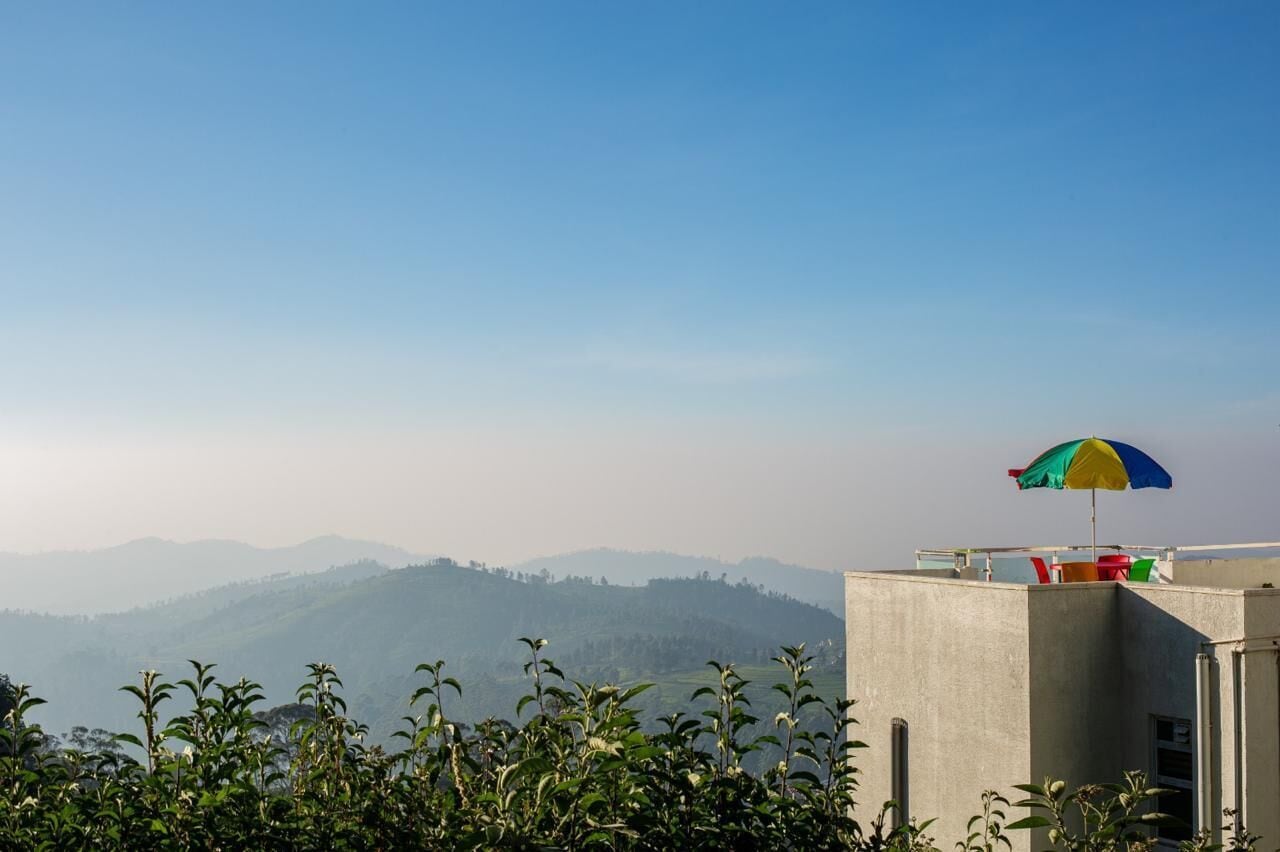 A rooftop with a colorful umbrella, a concrete structure, and a view of distant hills.