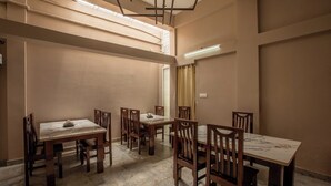 A room with four wooden tables and chairs, a marble floor, and a high ceiling with exposed ductwork. - Paradise Point Ooty (Coonoor)