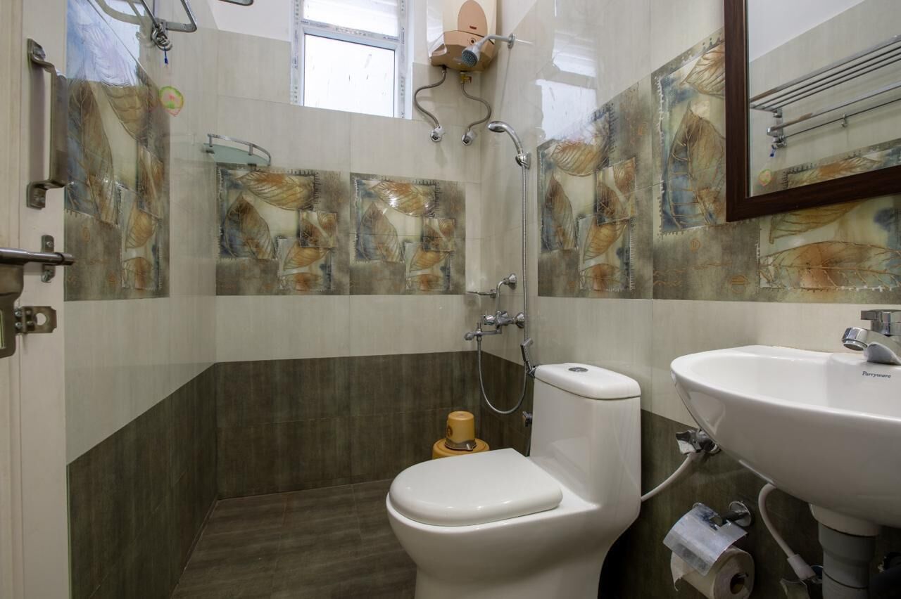 Une salle de bain comprenant des toilettes, un lavabo et une douche. Les murs sont recouverts de carreaux formant des motifs abstraits.