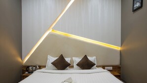 A modern hotel room with a neatly made bed, two pillows, a bedside table with a lamp, and a wall-mounted light fixture. - Paradise Point Ooty (Coonoor)