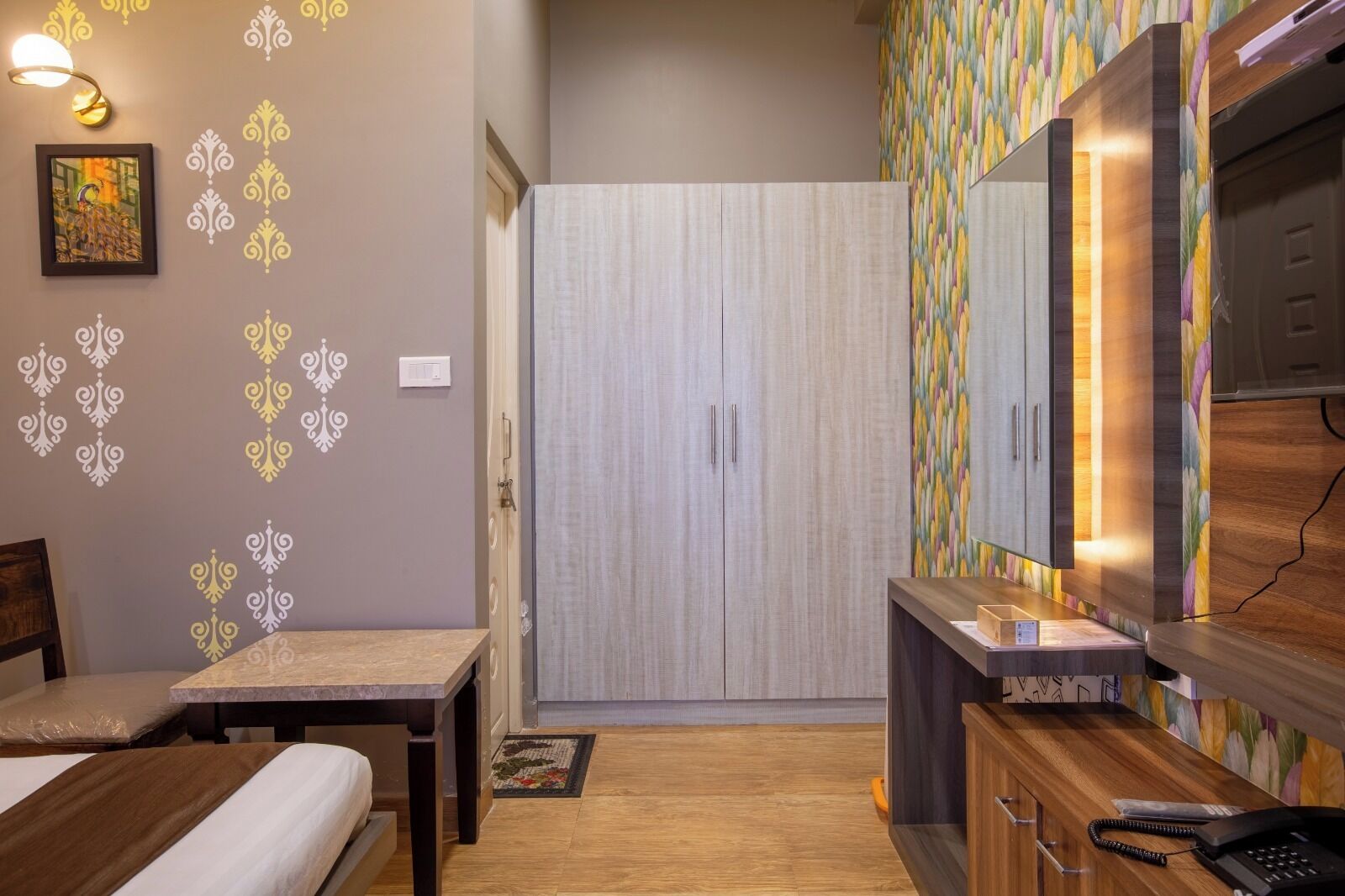 Een kleine slaapkamer met een bed, bureau, kast en spiegel.