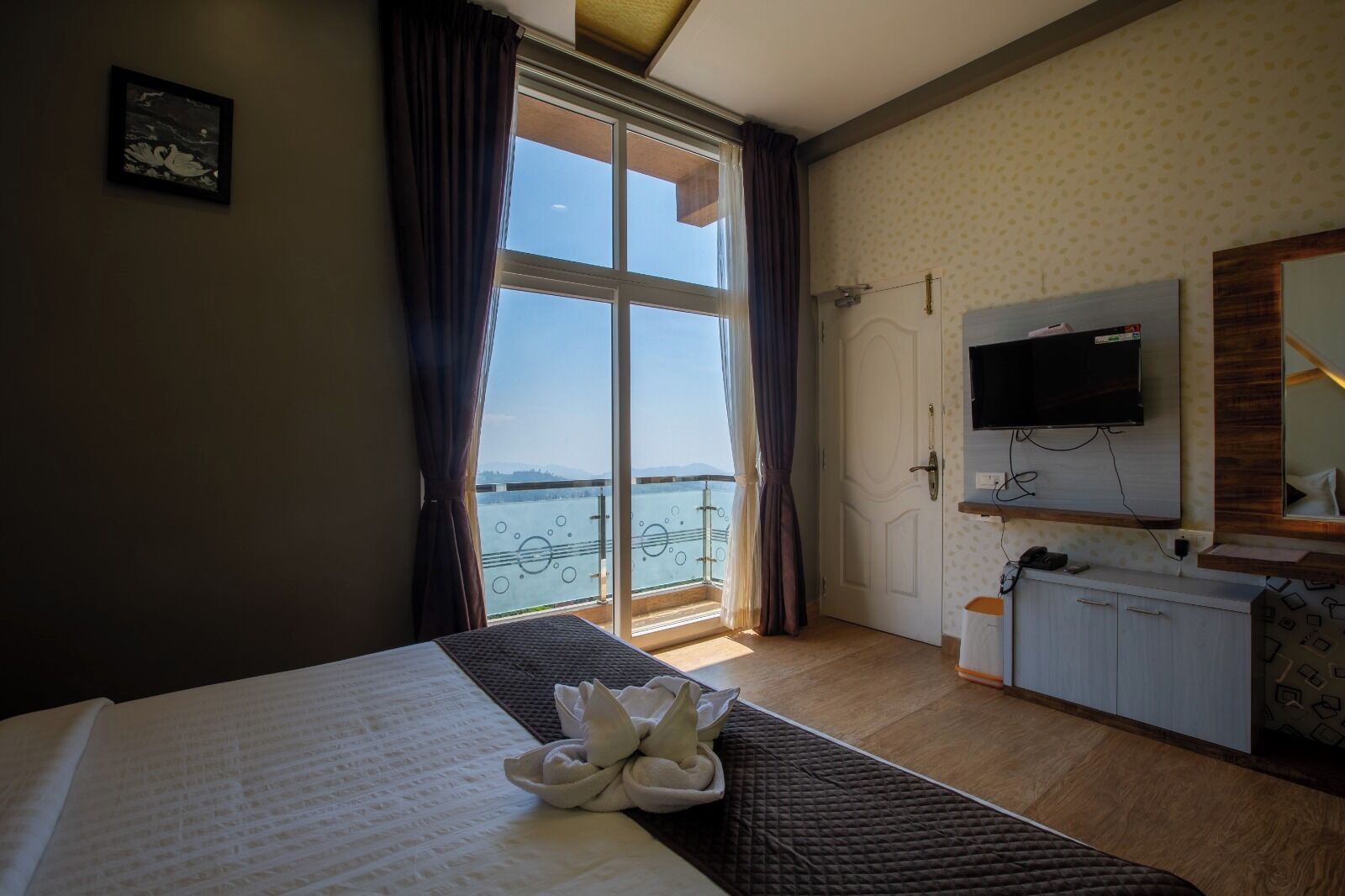 Een hotelkamer met een bed, bureau, televisie en een balkon met uitzicht op het water.