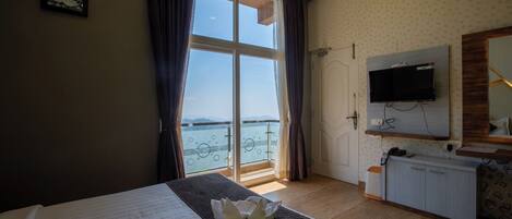 A hotel room with a bed, a desk, a TV, and a balcony with a view of the water.